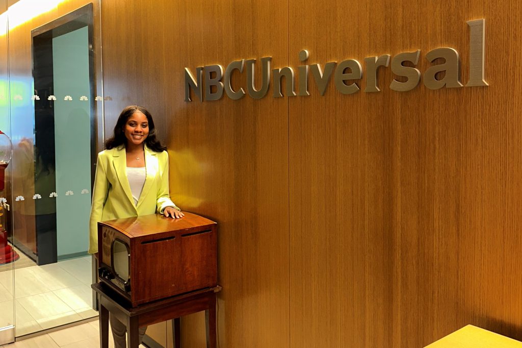 Taylor Washington stands next to NBC Universal building signage.