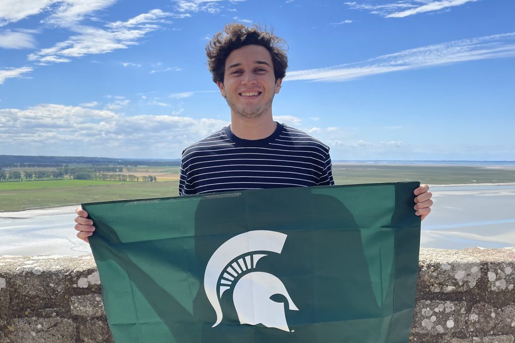 A student holds a Spartan flag while abroad in France.
