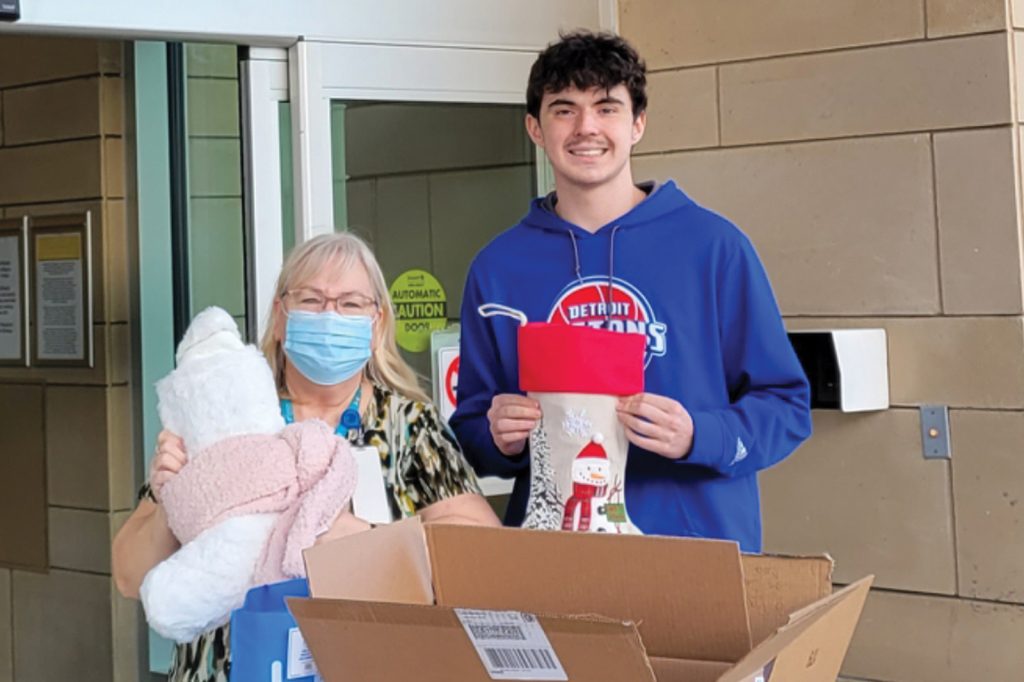 Jacob Weber and a woman hold holiday stockings while standing near a box of donated goods.