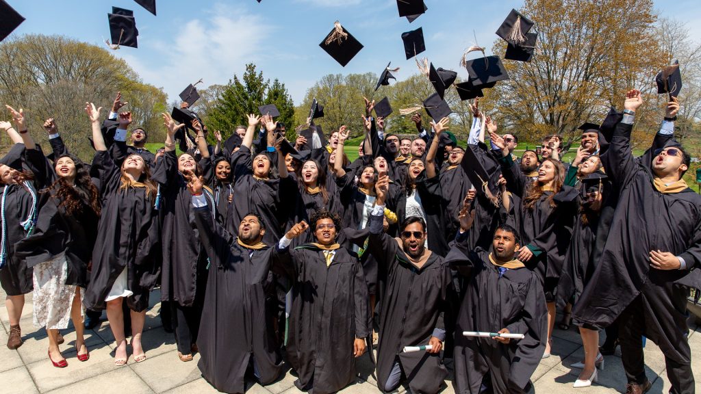 Broad Spartan MBA students wear graduation gowns and toss their caps into the air.