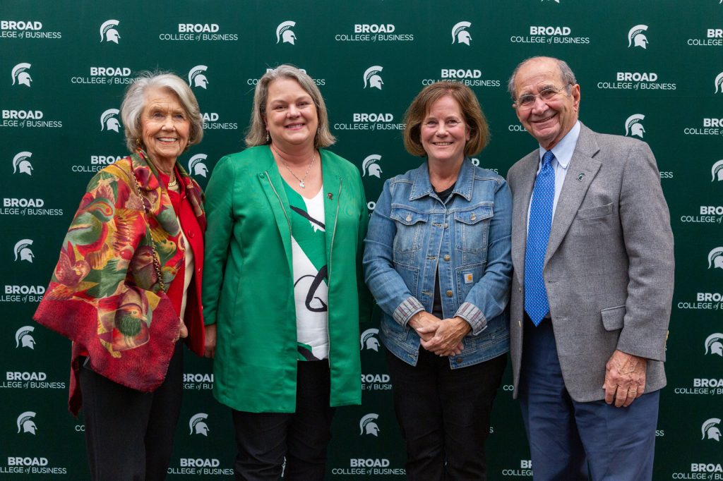 Jeannie James, Judith Whipple, Linda Hubbard and Ed James pose for a picture at the 2023 Warrington Lecture in front of a Broad College braded backdrop.