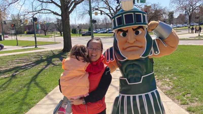 Yuxuan Gao and her daughter posing with Sparty outside on a sunny day
