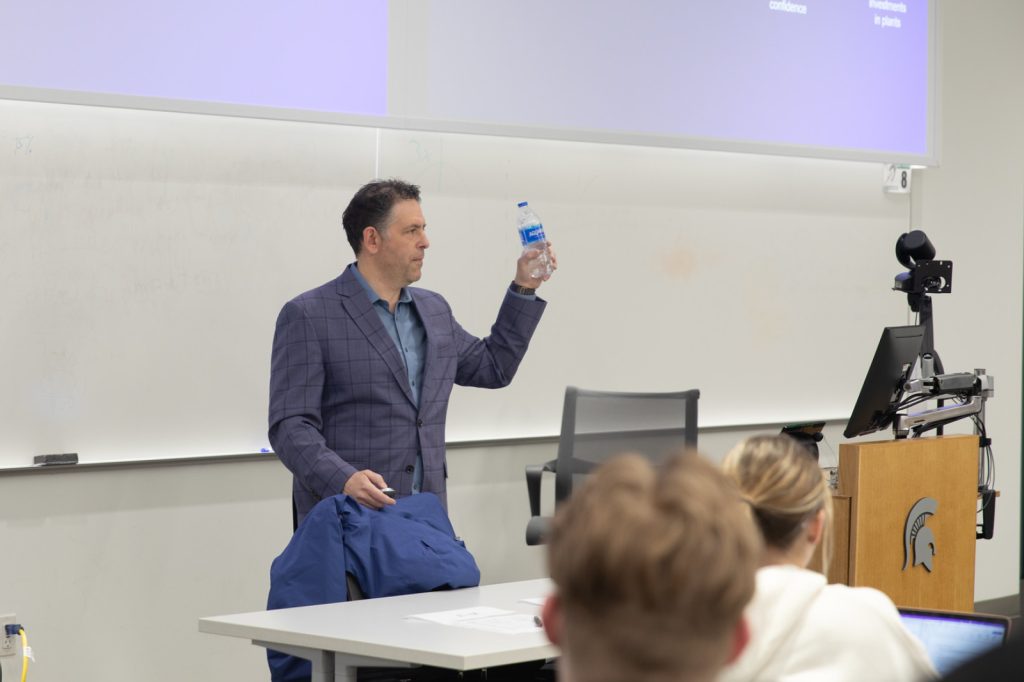 David Feber holds a single-use plastic water bottle while presenting to the Broad class.