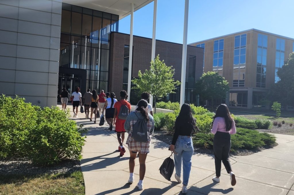 Students walk into the Minskoff Pavilion's main entrance off Shaw Lane on a sunny, summer day.