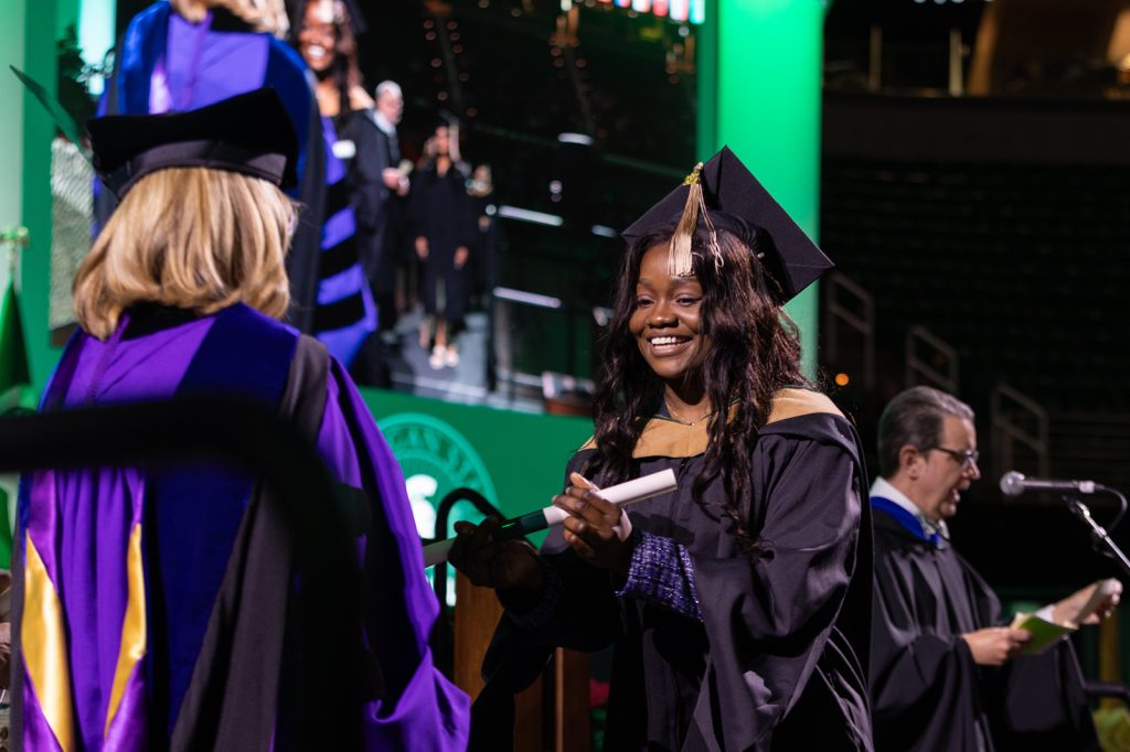 A Broad Spartan smiles while crossing the stage at commencement and receiving a diploma from Interim President Woodruff.