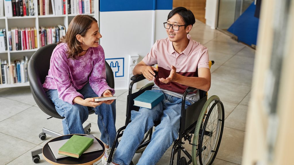 Stock image showing disability inclusion in the workplace, one person in wheelchair talking with another person.