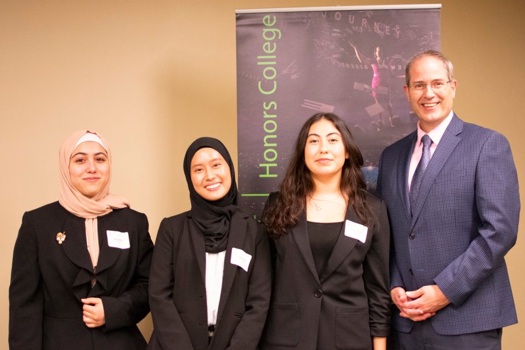 Three students pose with Chris Long after presenting their winning work on classroom implications of AI plagiarism and fabrication.