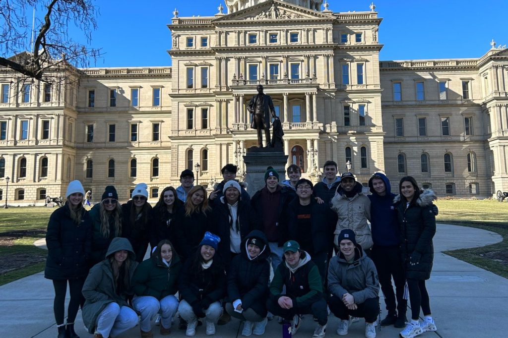Members of the MSU student organization Phi Chi Theta pose in front of the Michigan State Capitol building.