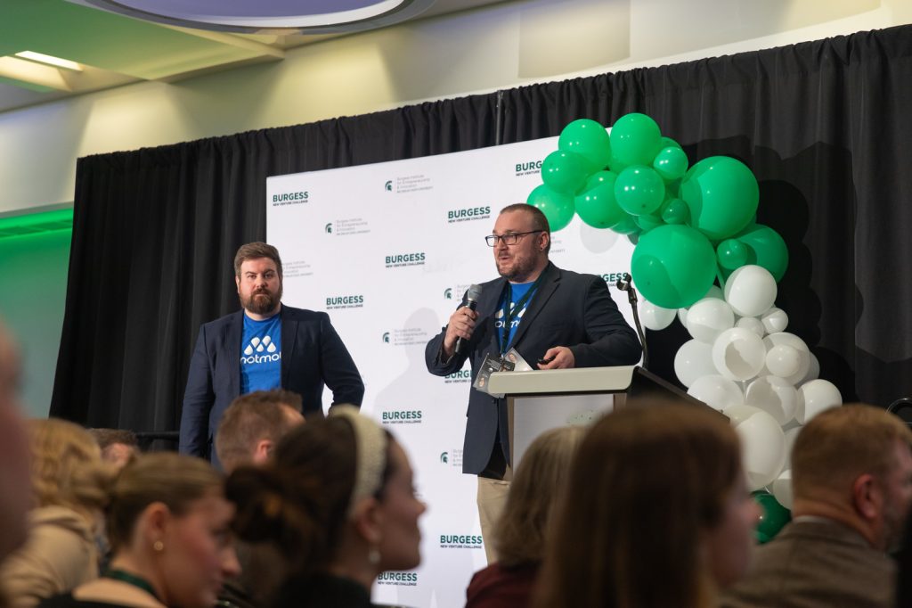 Two Spartan entrepreneurs stand on a stage at the 2024 Burgess New Venture Challenge.