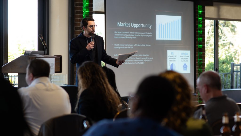 An Executive MBA student holds a microphone and papers while presenting a business idea at the 2024 pitch competition.