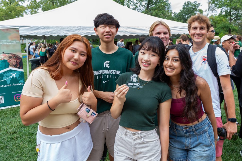 A group of students pose and smile. One holds a Broad College of Business laptop sticker.