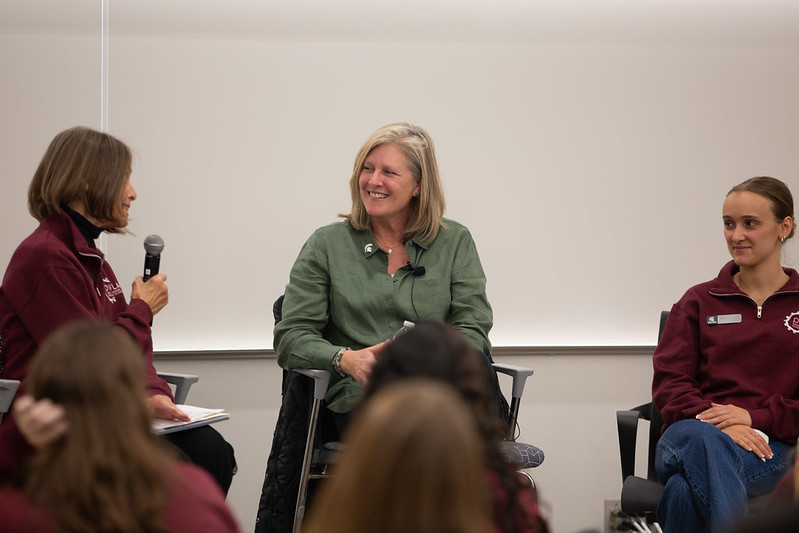 Three women sitting on a panel, one speaking into a microphone