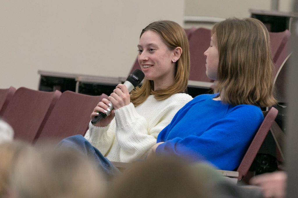 Two students sitting down, one holding microphone