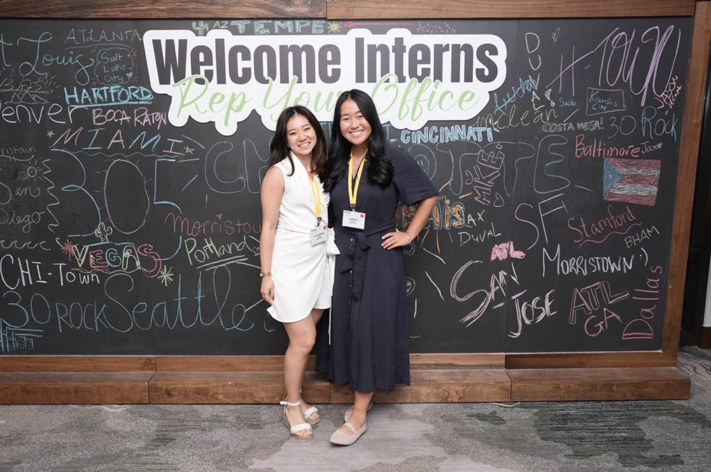 Two women posing in front of a sign that reads 