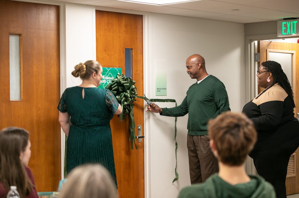 Two people cutting a green ribbon on a door