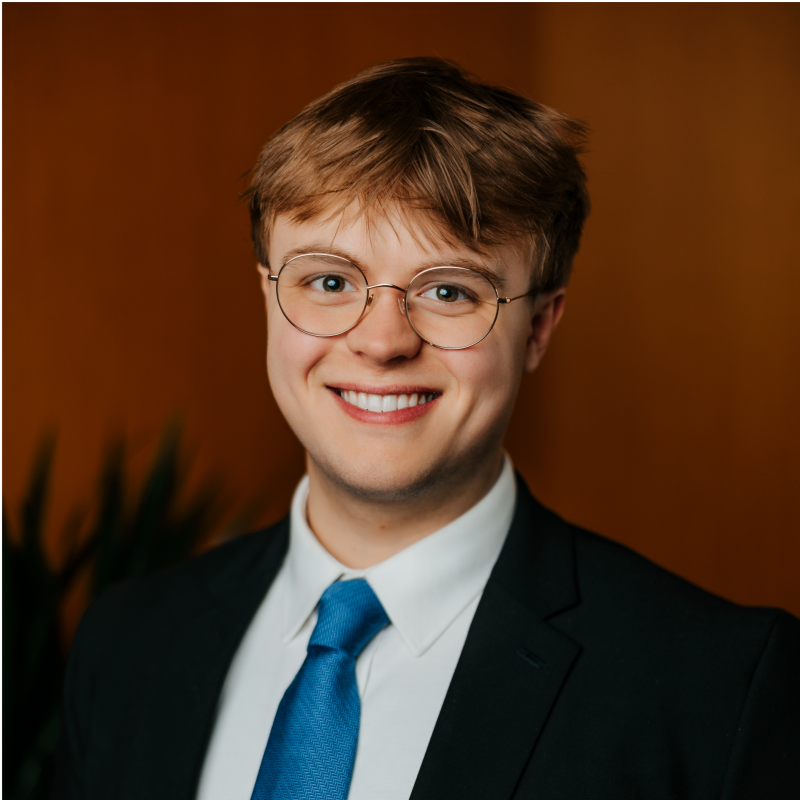 Student wearing a suit, blue tie and jacket in front of orange background