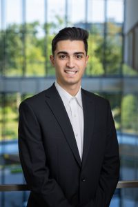headshot of a smiling man with light skin and dark hair wearing a business suit