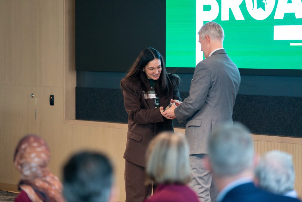 A student receives an award on stage during the Celebrate Broad ceremony as attendees look on.