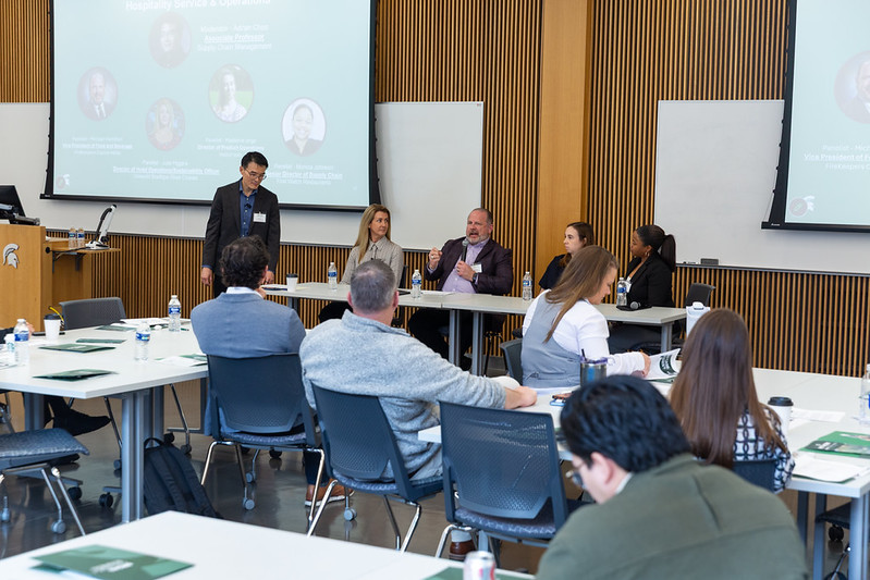 Panel speakers sitting at the front of the room speaking with symposium attendees.