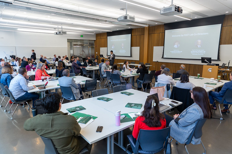 FAST Symposium participants sitting at tables spread out in a room, listening to a speaker at the front of the room.