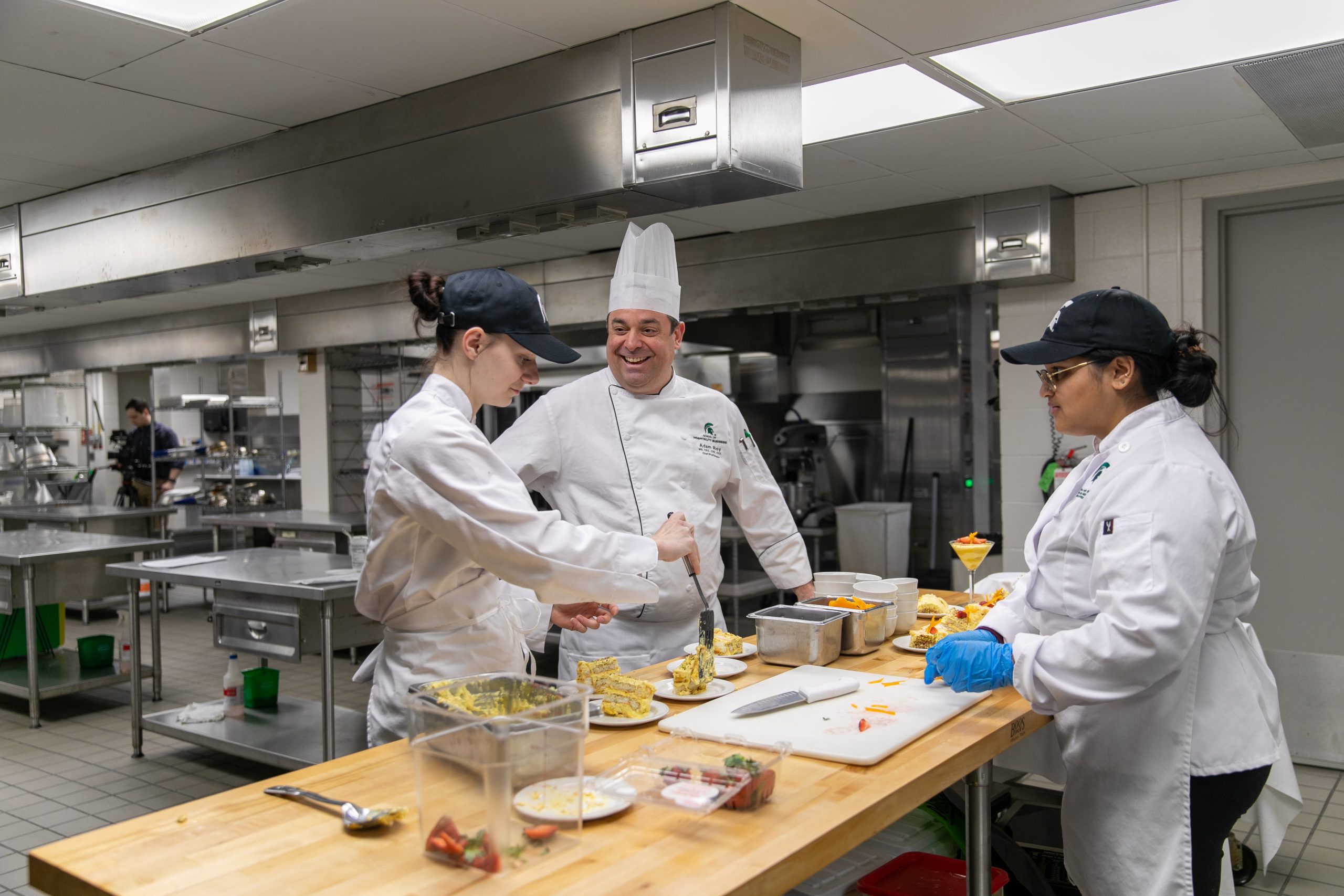 A head chef instructs two other chefs in an industrial kitchen.