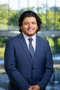 headshot of a Mexican American man wearing a dark blue suit and tie. 