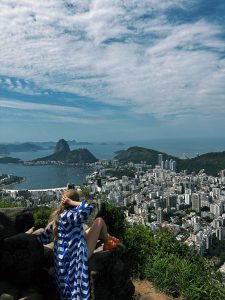 back of a woman in the foreground, she looks at a city scape on the coast next to the water in the background