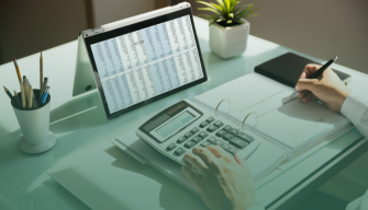 Master's in Accounting student using a calculator beside a tablet displaying financial data and spreadsheets on a desk.