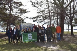 Students pose with a block "S" flag during their parks project at a park
