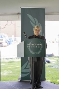 President Simon stands at a podium. The podium banner reads, "Michigan State University"