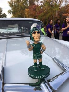 A Sparty bobble head sits on the hood of a car in the 2017 homecoming parade.