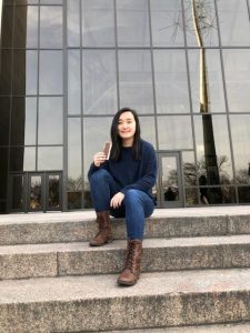 Demi Yang sits on the cement steps of a building and holds an ice cream sandwich 