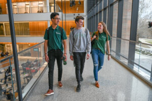 Three Broad undergraduate students walking in the Minskoff Pavilion, wearing Michigan State University-branded apparel.