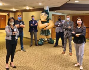 Executive MBA students pictured in the Henry Center wearing protective masks during this year's residency week, posing with arms crossed near an inflatable Sparty.